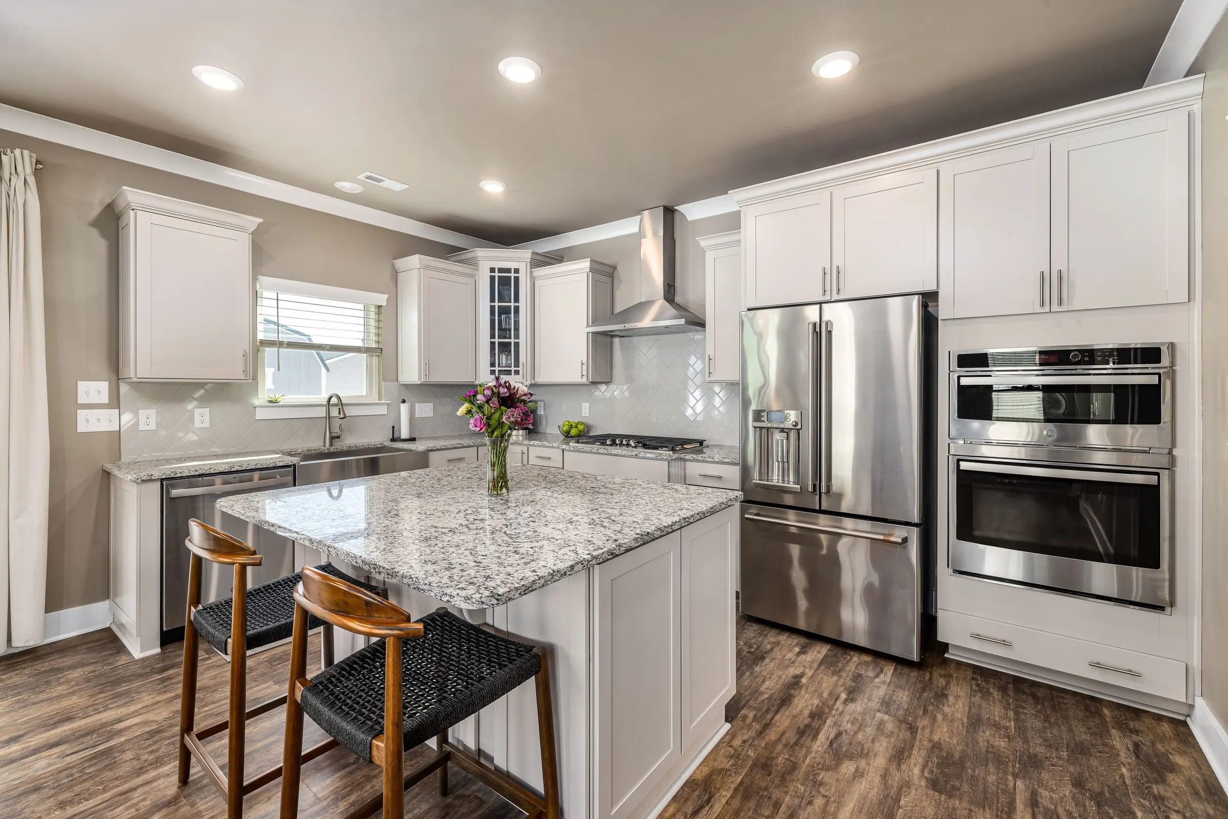 A remodeled kitchen with a granite island, bar stools and stainless steel appliances