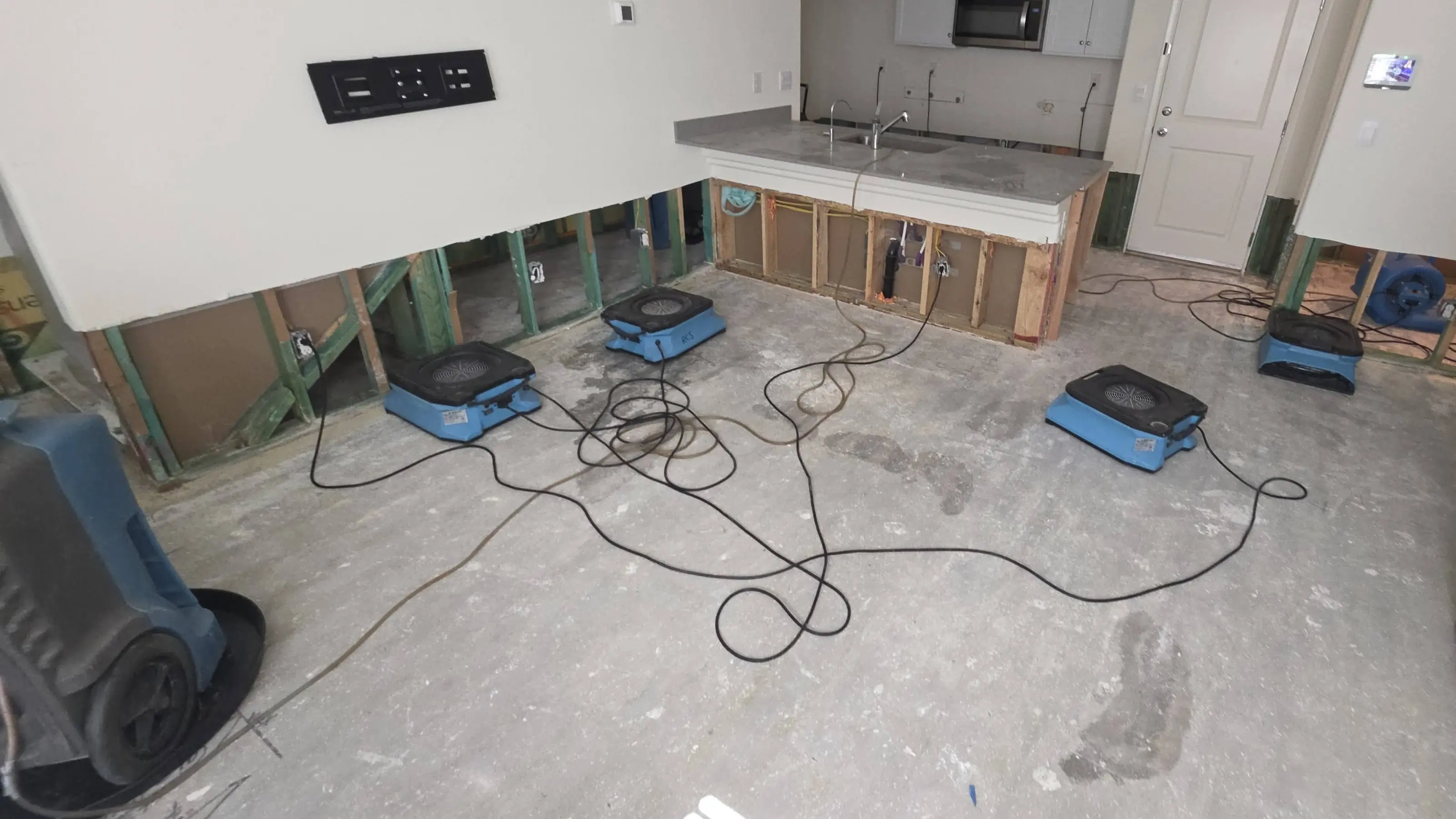 A kitchen and living area with the lower wall cut out and air movers on a bare slab